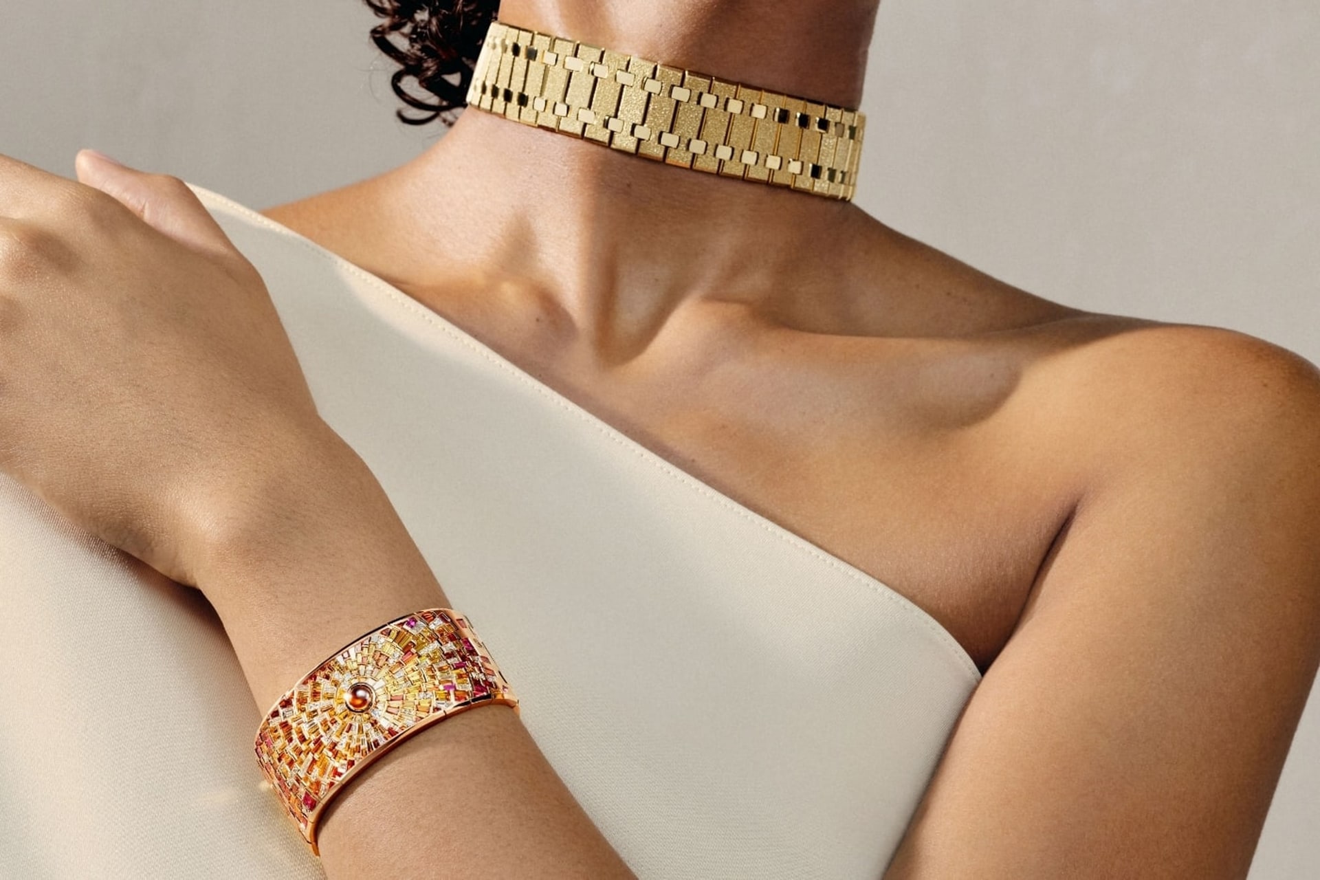 Ein Choker aus Frosted Gold am Hals und die Sunburst-Manschette am Handgelenk einer Frau in einem cremefarbenen Oberteil mit einer Schulter