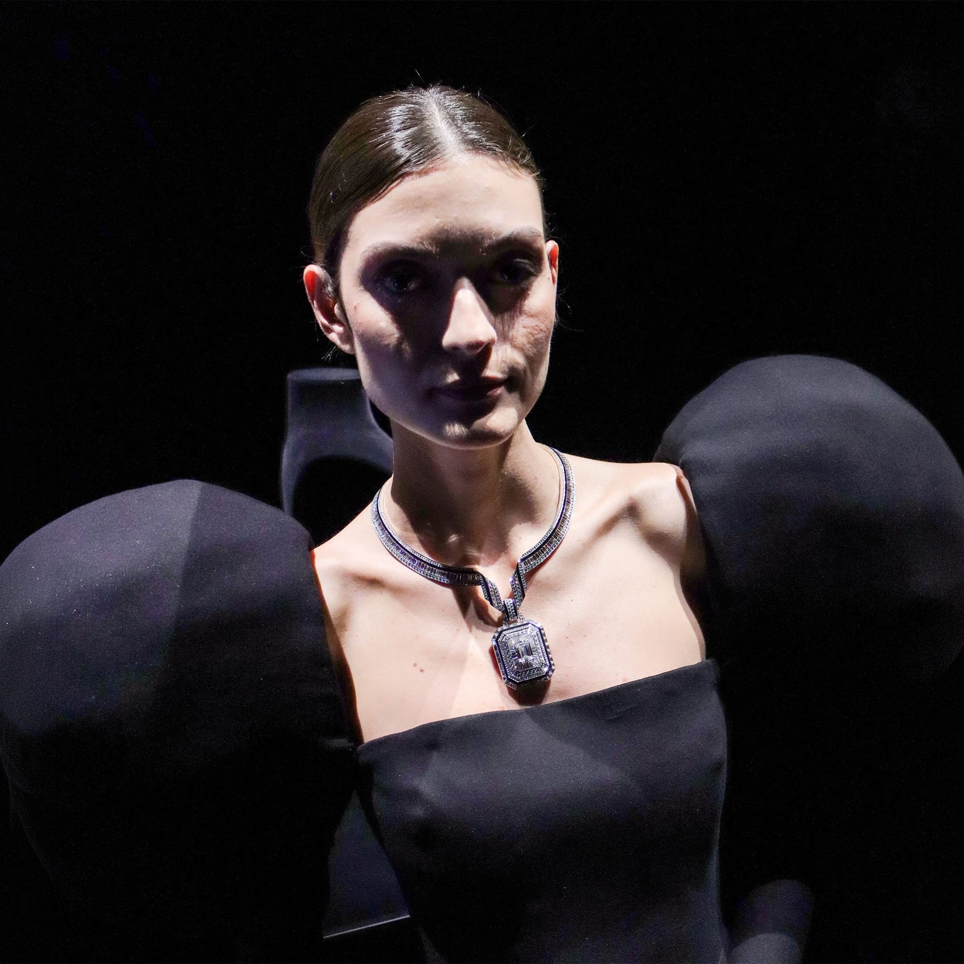 A model wears The Address with a black dress with large round sleeves, in a spotlight against a black background